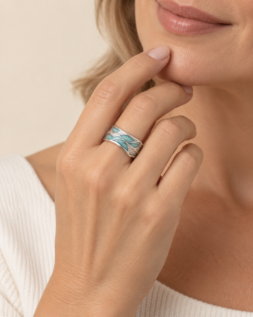 A close-up lifestyle shot of a woman wearing a silver band ring with a textured, layered turquoise and white pattern, resting on her index finger.