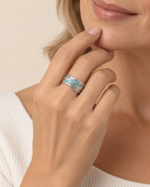 A close-up lifestyle shot of a woman wearing a silver band ring with a textured, layered turquoise and white pattern, resting on her index finger.