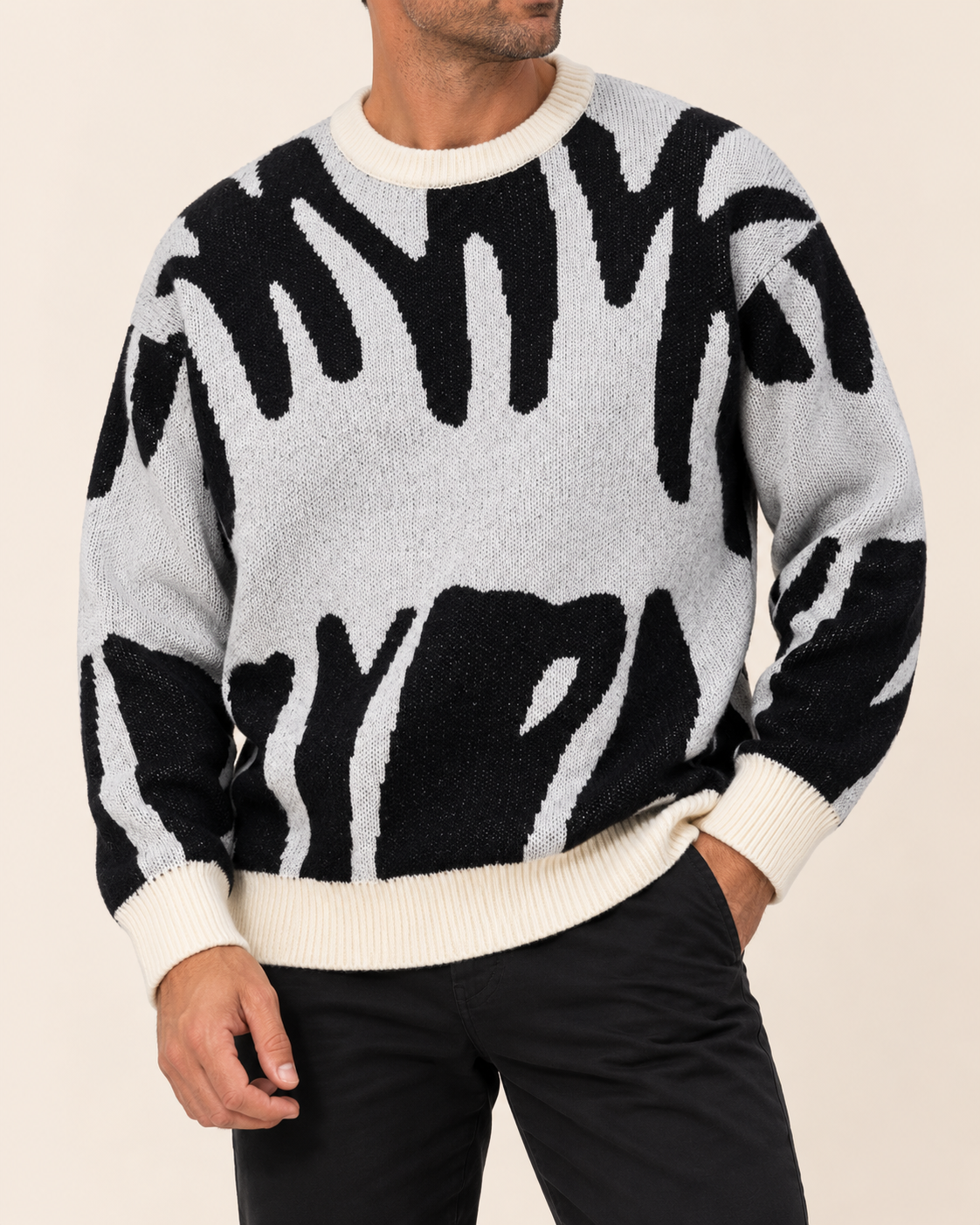 A man wearing a black and off-white zebra-patterned knit sweater with cream ribbed collar, cuffs, and hem, paired with black pants, against a solid light beige background.