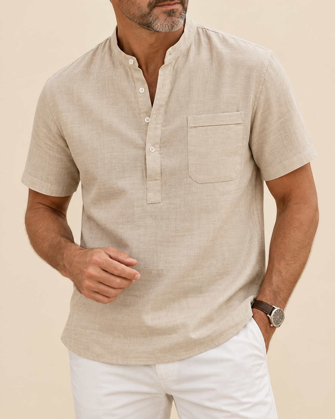 A man wearing a light beige linen short-sleeve henley shirt with a chest pocket, paired with white pants, against a solid beige background.