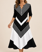 A woman wearing a black and white geometric midi dress with three-quarter sleeves, a V-neckline, and side pockets, set against a solid beige background.
