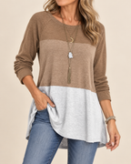 A woman wearing a color-blocked long-sleeve tunic top with a brown upper section, a taupe middle band, and a light gray lower panel, paired with blue jeans against a plain beige background.