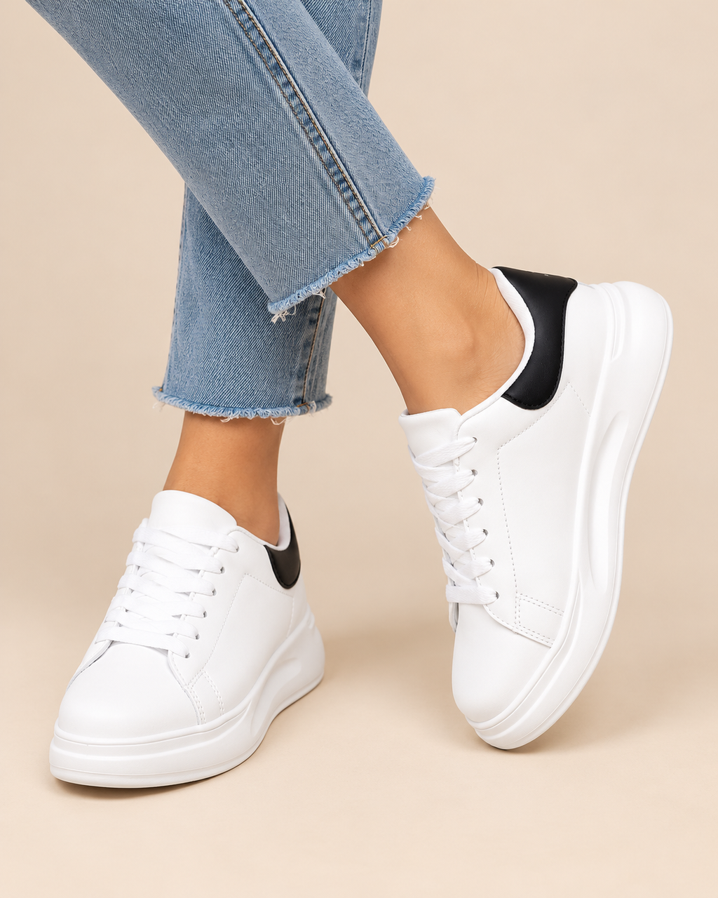 White platform sneakers with black heel accents, shown on a model wearing light blue frayed-hem jeans against a beige background.