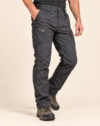 A person wearing dark charcoal cargo pants with brown hiking boots, shown from the waist down against a plain beige studio background.