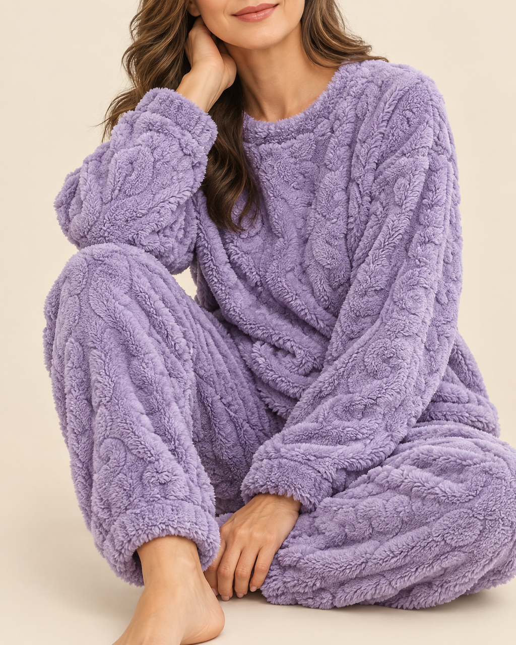 A woman wearing a cozy, textured lavender fleece pajama set with a cable-knit pattern, sitting against a solid beige background.