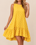 A woman wearing a sleeveless yellow high-low dress with white polka dots and a ruffled hem, photographed against a plain beige studio background.