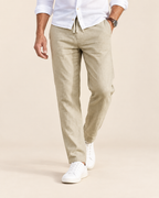 A man wearing beige drawstring trousers, a white button-down shirt, and white sneakers, shown from the waist down against a light beige studio background.