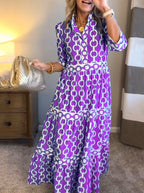 Woman wearing a purple and white patterned dress holding a gold handbag indoors.