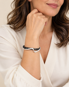A close-up of a woman wearing a sculptural black and white wavy bracelet on her wrist, dressed in a white blouse.