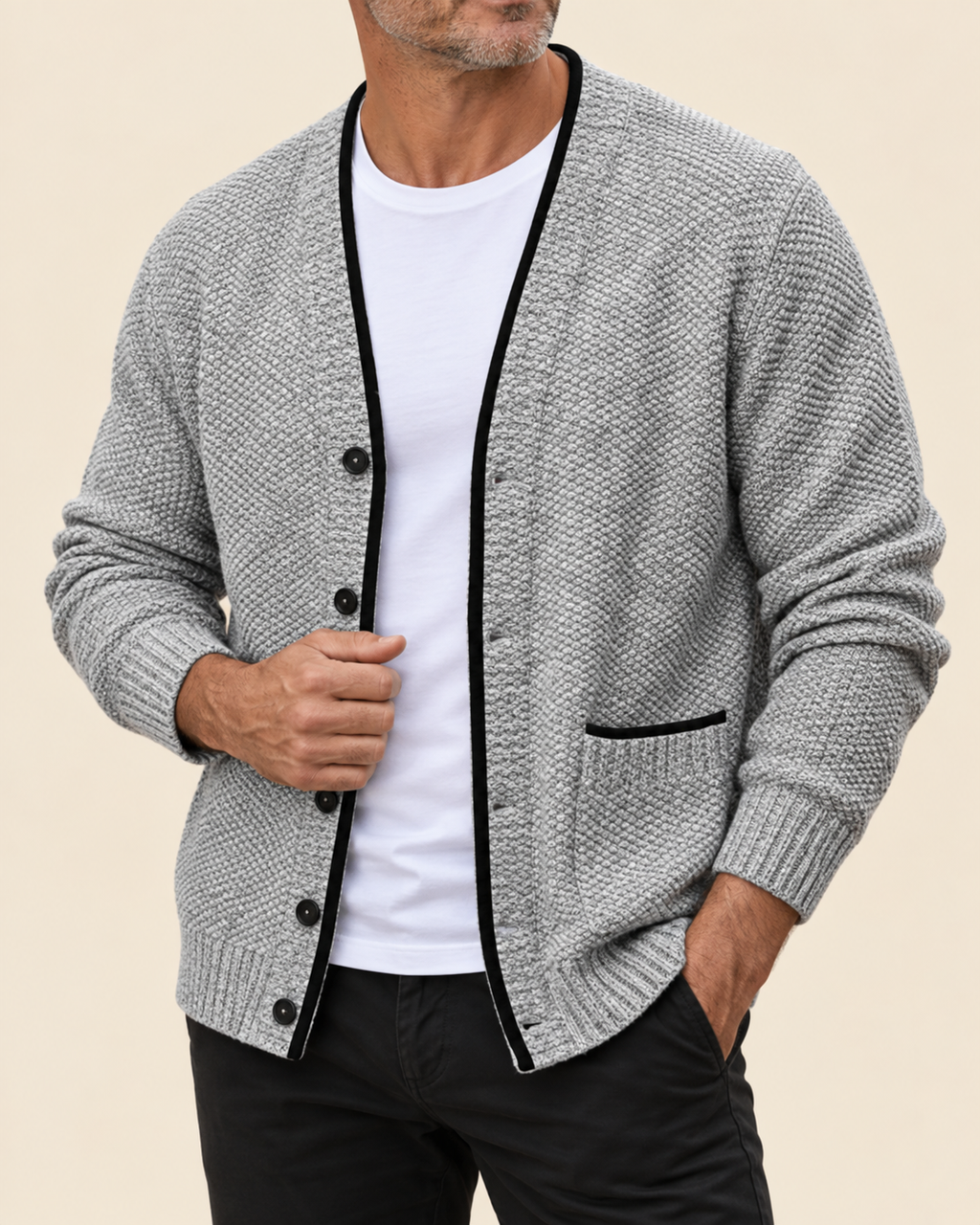 A man wearing a gray textured knit cardigan with black trim over a white t-shirt and black pants, shown from the chin down against a solid beige background.