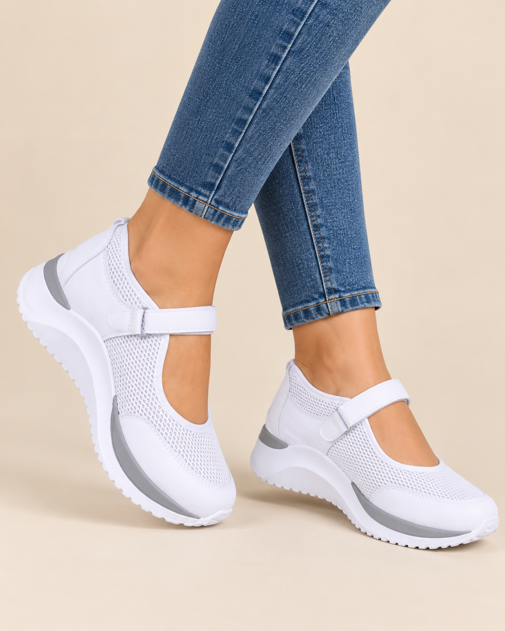 White mesh Mary Jane-style slip-on shoes with hook-and-loop straps and gray side accents, shown on a model wearing blue jeans against a light beige studio background.