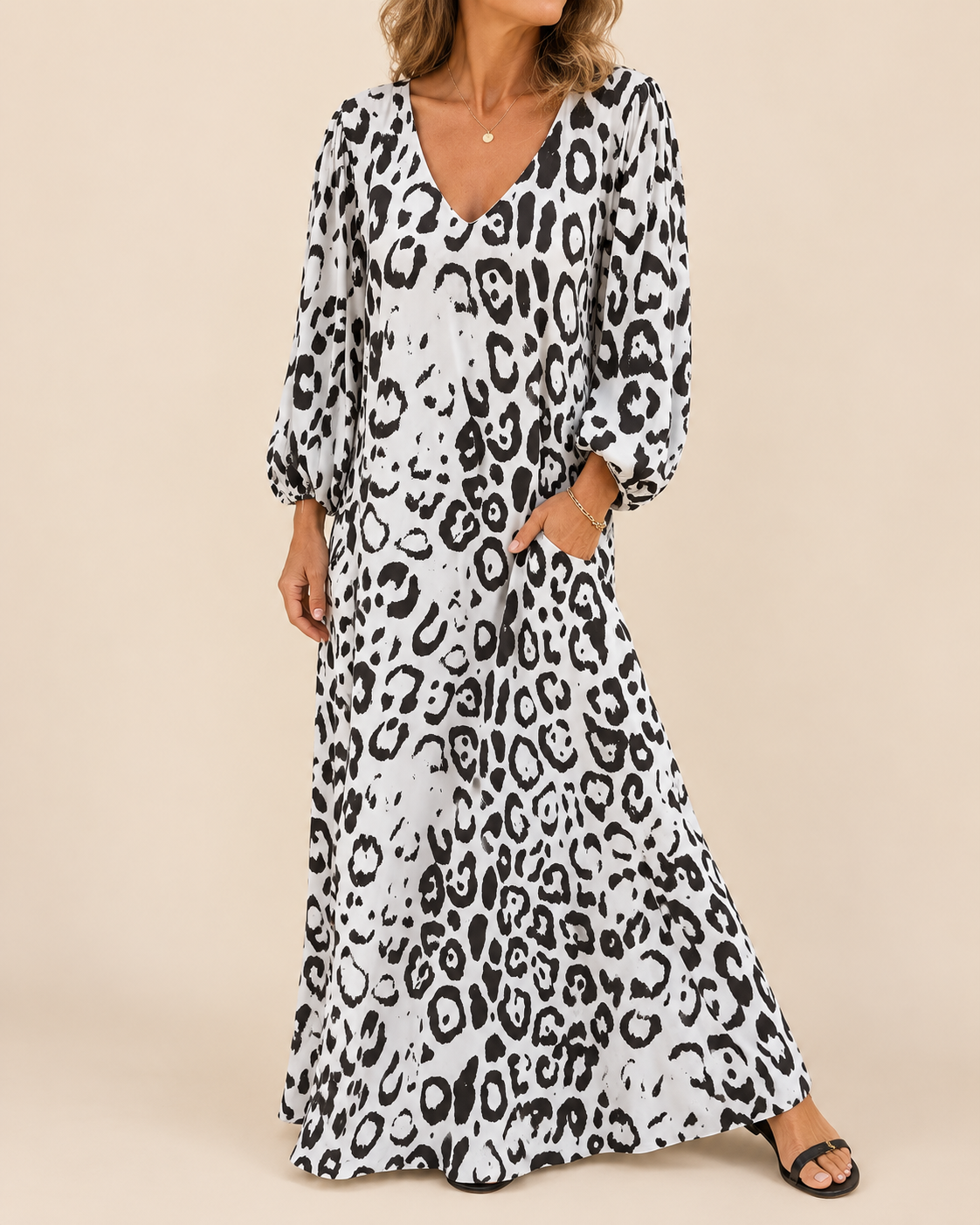 A woman wearing a long white maxi dress with a black leopard print pattern, featuring balloon sleeves and a V-neckline, standing against a solid beige background.