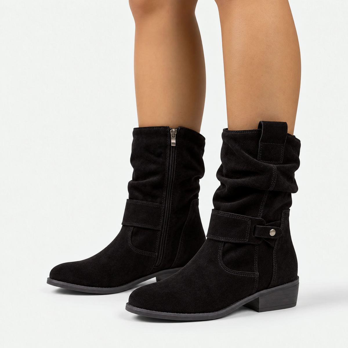 Black slouchy ankle boots with a side zipper and a silver buckle detail, shown on a model's feet against a light gray background.