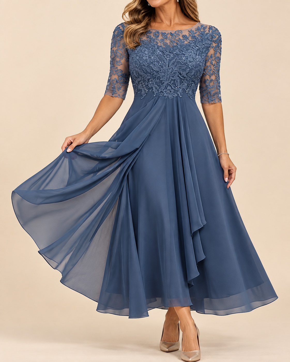 A woman modeling a dusty blue A-line midi dress with a lace bodice and sheer lace sleeves, holding out the flowing chiffon skirt against a solid beige background.